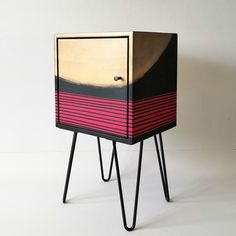 a black and pink cabinet sitting on top of a metal stand next to a white wall