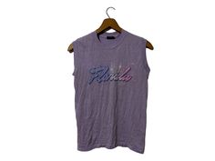 "1980's Vintage Florida Spring Break Beach SURF Vacation Sleeveless T-shirt Rad Beachwear Light Purple with Graphic Adult Medium Size: The tag says Adult Medium (vintage sizing runs small) Close to Small modern size Color: Light Purple Measurements: item lying flat,  17\" wide (armpit to armpit)  22\" length Brand: Sneakers Material: 500% cotton 50% Polyester made in USA Condition: This item is vintage and has been previously loved. There is a faintly bleahced spot at the bottom and a tiny hole Vintage Sleeveless T-shirt With Graphic Print, Vintage Tank T-shirt For Summer, Sleeveless Cotton T-shirt For Beach, Vintage Tank Top For Spring Streetwear, Vintage Cotton Muscle Tee For Summer, Vintage Cotton Muscle Tee For Spring, Retro Sleeveless Summer T-shirt, Sleeveless Beach T-shirt For Summer, Retro Crew Neck Tank Top For Summer