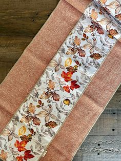 an orange and white table runner with autumn leaves on it, sitting on a wooden surface