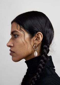 a woman with black hair wearing large hoop earrings and a black turtle neck sweater is looking off to the side