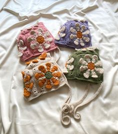 four crocheted hats with flowers are on a white sheet, and one has a knot at the end