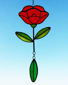 a stained glass rose hanging from a chain on a blue sky background with green leaves