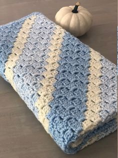 a blue and white crocheted blanket next to a pumpkin