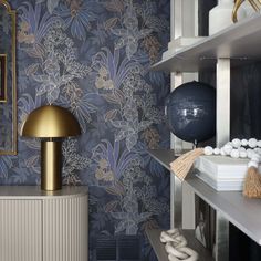 a room with blue and white wallpaper, gold accents and a large lamp on the shelf