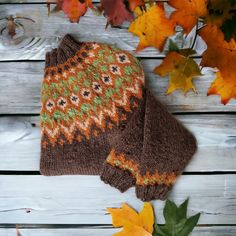 a knitted sweater and hat sitting on top of a wooden table next to autumn leaves