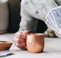 a person holding a copper mug and playing cards