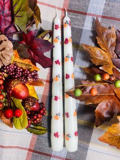 two candles sitting on top of a table next to autumn leaves and pumpkins,