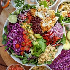 a large salad with lots of different toppings in bowls on top of a wooden table