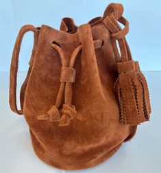 This women's crossbody bucket bag is handmade from vegetable tanned European caramel brown suede. The bag has an adjustable shoulder strap and two removable tassels. The bag is unlined and closes with the drawstring cord. The suede is buttery soft and has a rich caramel brown colour. It's lightweight and will be perfect for any occasion.  The bag measurements: 6.5 x 8.5 x 6.5 inch. Made of genuine vegetable tanned cow suede.  Colour: Caramel Brown. Handmade in United States. Suede Bucket Bag With Removable Pouch, Suede Bucket Shoulder Bag With Removable Pouch, Brown Suede Bucket Bag For Everyday Use, Brown Suede Bucket Bag For Daily Use, Suede Bucket Bag With Adjustable Strap For Travel, Travel Suede Bucket Bag With Adjustable Strap, Suede Bucket Bag For Travel, Daily Use Suede Bucket Shoulder Bag, Suede Bucket Bag With Removable Pouch For Travel