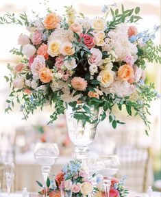 a vase filled with lots of flowers sitting on top of a table next to two wine glasses