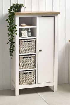 a white cabinet with three wicker baskets on the bottom and one door open, next to a potted plant