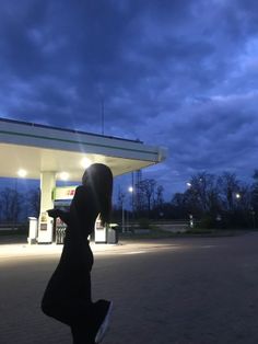 a person standing in front of a gas station at night with their shadow on the ground