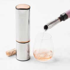 a wine glass being filled with liquid next to a metal tube and corkscrew