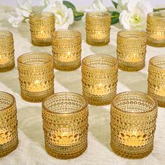 many glasses are lined up on a table with white flowers in the backgroud