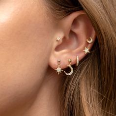 a close up view of a woman's ear wearing gold stars and moon earrings