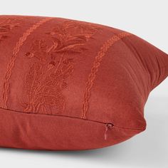 a red pillow with an embroidered design on the front and back, sitting on a white surface