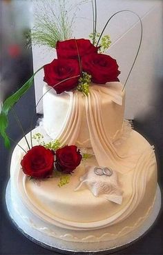 a three tiered white wedding cake with red roses on top