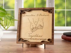 a wooden sign with two hands holding each other on a table next to a potted plant