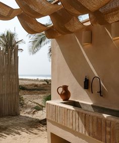 a sink under a wooden roof next to a beach with palm trees and the ocean in the background