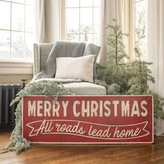 a red merry christmas sign sitting on top of a wooden floor next to a chair