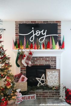 a decorated christmas tree in front of a fireplace with joy written on the mantel