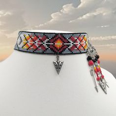 This choker has a diamond shaped center with adornments. It has a metal arrow dangling from the bottom center. After the center it gets a little complicated as the arrows are in one direction and the black lines that define the arrows go in other direction. After that they all go in the same direction, but the last arrow on the very end shoots in the other direction. It has a matte glazed lustered grey background that has a slight blue tint. The other colors are black, dark red, red, orange, yellow and white. It is 12 7/8 inches long. The earrings have five strands with arrows on the outside strands and the center has an arrow like the one on the choker. The rest are beads and rondelles. Adjustable Triangular Beaded Jewelry, Adjustable Triangle Beaded Jewelry, Necklaces Ideas, Seed Bead Jewelry Patterns, Native Crafts, Loom Bracelet Patterns, Loom Bracelet, Beading Jewelery, Bead Weaving Patterns