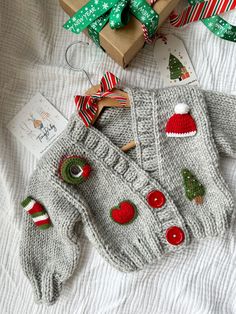 a knitted sweater with christmas decorations on it next to a present box and ribbon