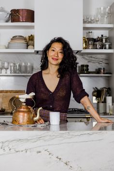 a woman standing in front of a counter with a tea pot and kettle on it