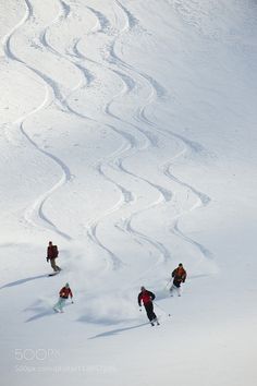 three skiers are skiing down a snowy mountain slope with tracks in the snow behind them