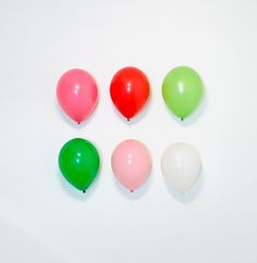 six balloons are arranged in a circle on a white surface, one is green and the other is red