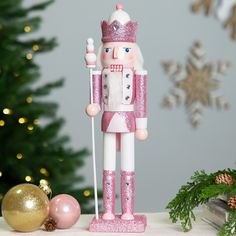 a pink and white nutcracker figurine next to a christmas tree