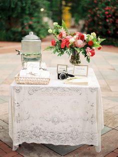 a table topped with a vase filled with flowers next to a white table cloth covered table