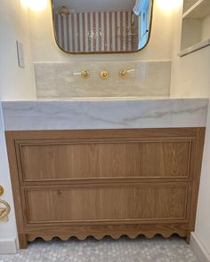 a bathroom vanity with marble counter top and gold faucet lights on the wall