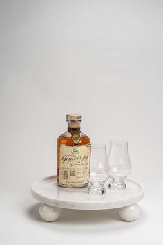 a bottle and two glasses sitting on a white table with a white background behind it