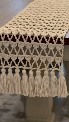 a white table runner with tassels on top of it and a wooden table in the background