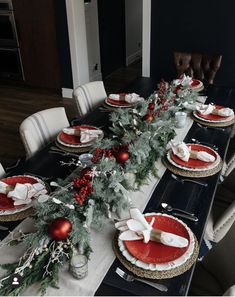 the table is set for christmas dinner with red and white plates, silverware and greenery