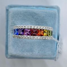 a rainbow colored diamond ring in a blue velvet box with white diamonds on the sides