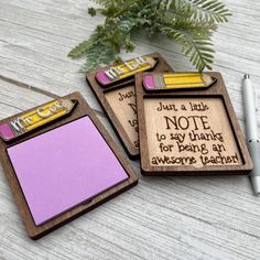 three wooden magnets with writing on them next to a pen and flower pot filled with greenery