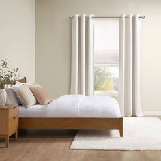 a bed with white sheets and pillows next to a wooden dresser in front of a window