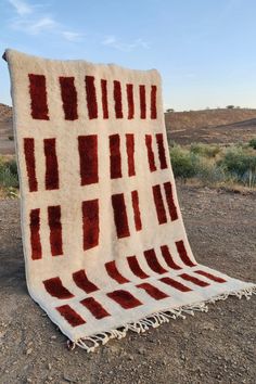 a red and white blanket sitting on top of a dirt field