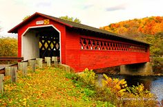 a red covered bridge over a river surrounded by fall colored trees and foliage in the background