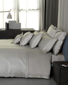 a bed with white sheets and pillows next to a night stand in front of a window