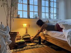 a woman laying on top of a bed next to a table with books and a lamp