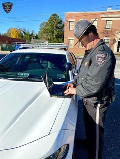 a police officer standing next to a white car and looking at the laptop screen that is open