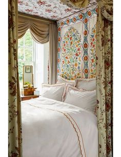 a bed with white sheets and pillows in front of a floral wallpapered headboard