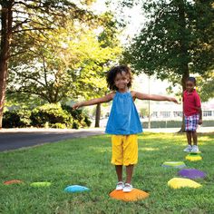 two young children playing in the grass with their arms spread out and one child standing on an obstacle