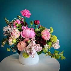 a white vase filled with lots of pink and green flowers on top of a table