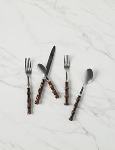 four forks and two spoons sitting next to each other on a white marble surface