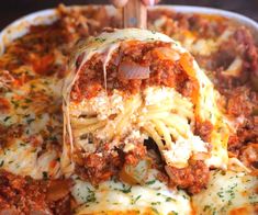 a person is scooping some food out of a casserole dish with meat and cheese