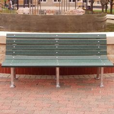 a green park bench sitting in front of a fountain on a brick walkway next to a building